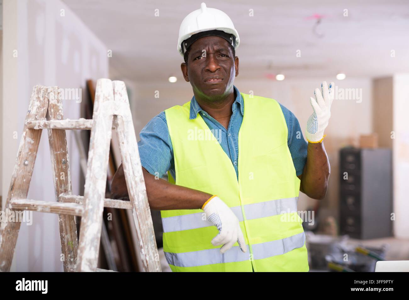 Portrait of disgruntled african american worker in yellow vest in cottage under construction Stock Photo
