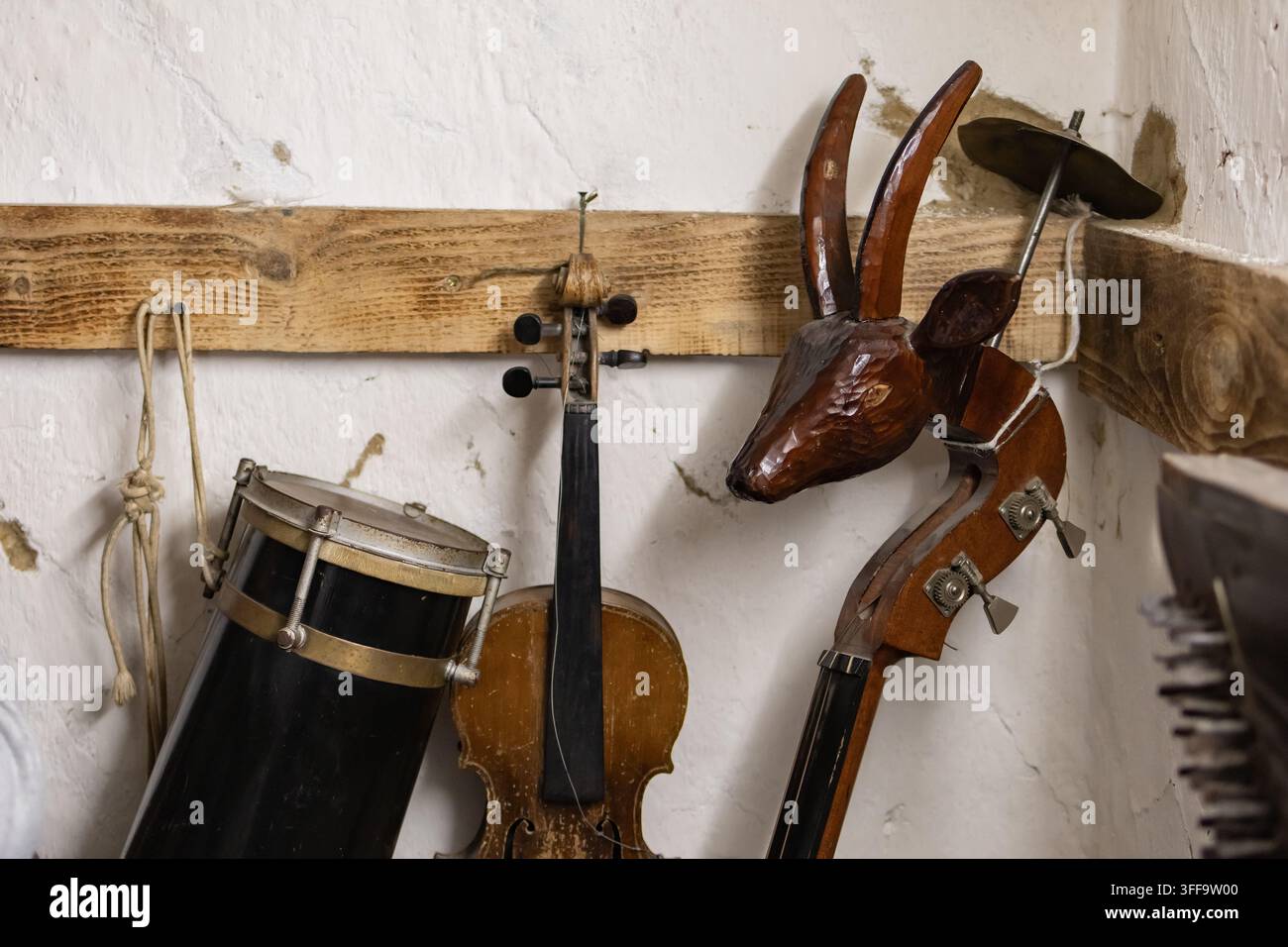 Collection of folk instruments hanging on a rustic wall including a drum a worn violin and a double bass with a carved animal head creating a nostalgi Stock Photo