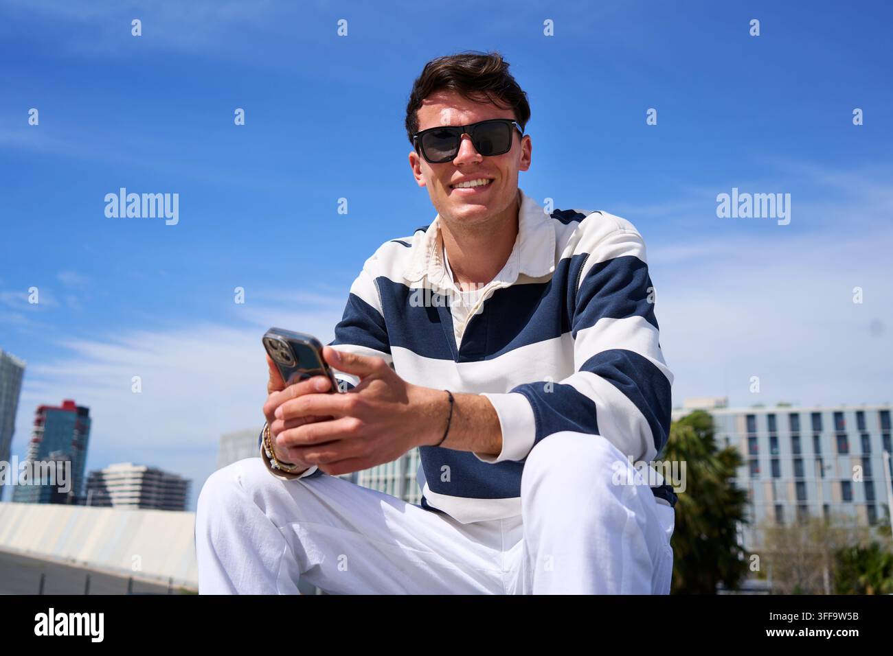 Young man smiling using smartphone in urban setting Stock Photo