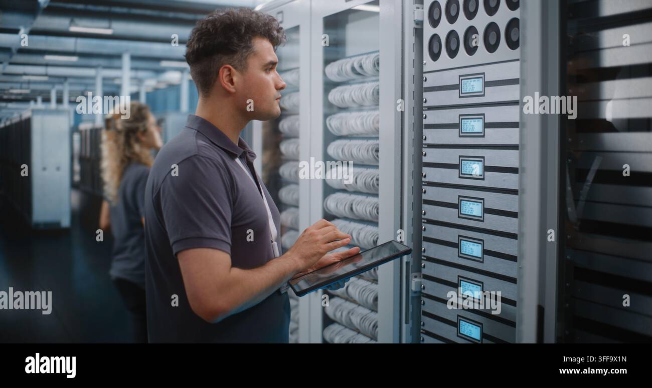 Focused Network Technician Holds Tablet Device while Verifying Server Rack Labels and Hardware Setup. Mobile Diagnostics and Structured Cabling Management Maintain Enterprise Cloud Performance. Stock Photo