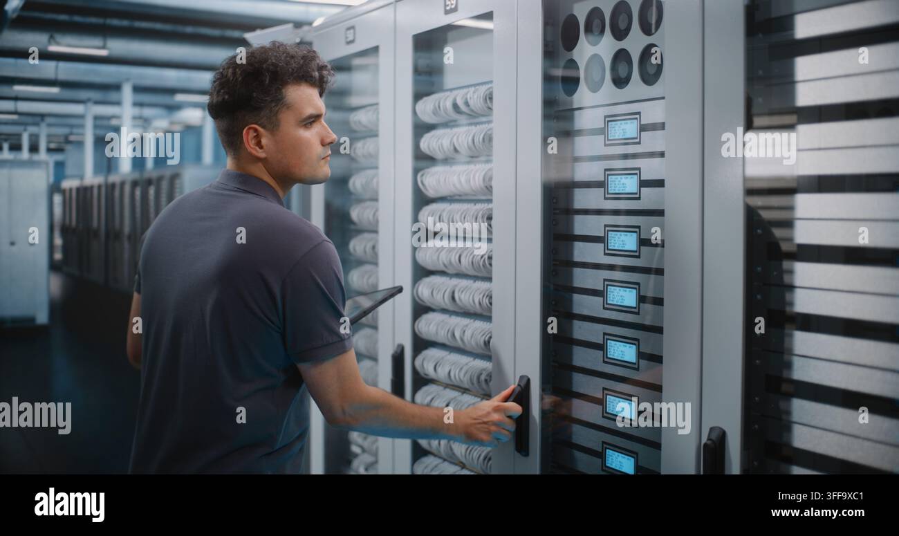 Focused Network Technician Holds Tablet Device while Verifying Server Rack Labels and Hardware Setup. Mobile Diagnostics and Structured Cabling Management Maintain Enterprise Cloud Performance. Stock Photo