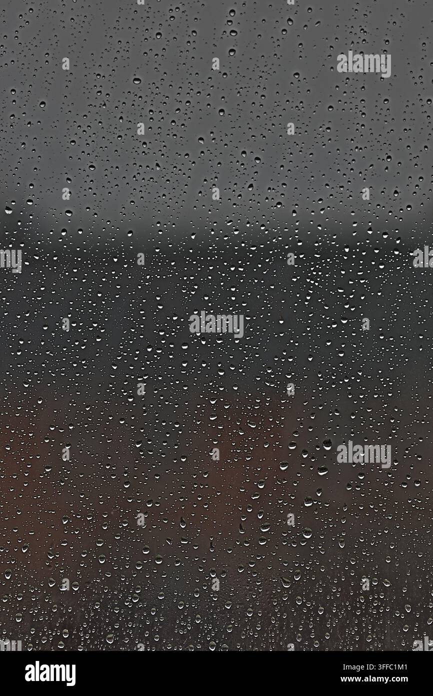 Raindrops on window glass during dark overcast storm. Stock Photo
