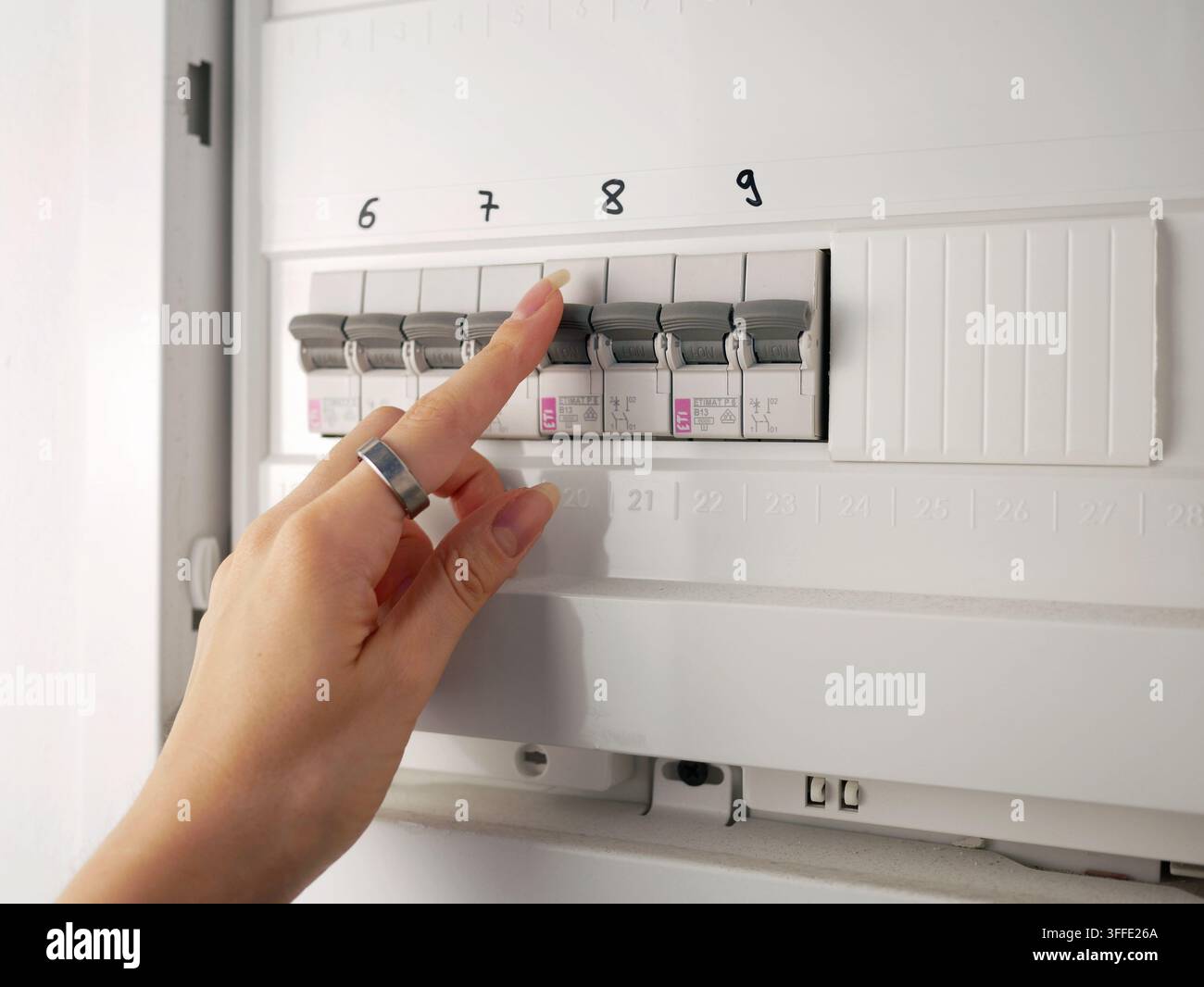 A hand checking circuit breakers in a residential electrical distribution panel with multiple labeled switches and protective devices Stock Photo