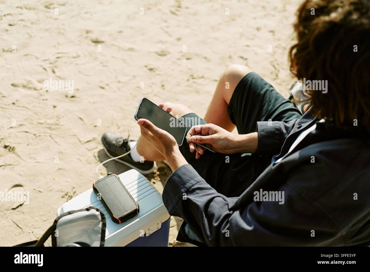 Man Charging Smartphone with Portable Power Bank on Beach Stock Photo