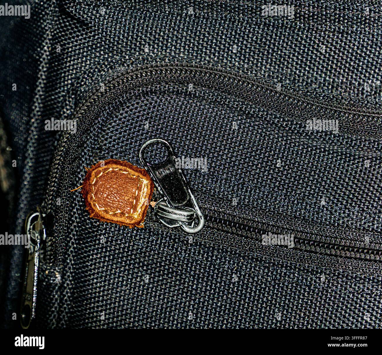 Macro close-up of a black fabric bag featuring a metal zipper, clasp, and distinctive brown leather zipper pull Stock Photo
