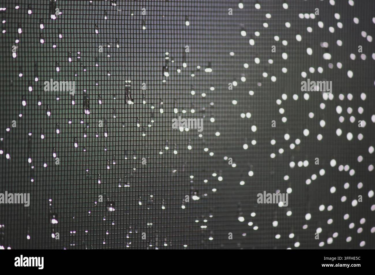 Raindrops and bokeh lights on window screen mesh at night Stock Photo