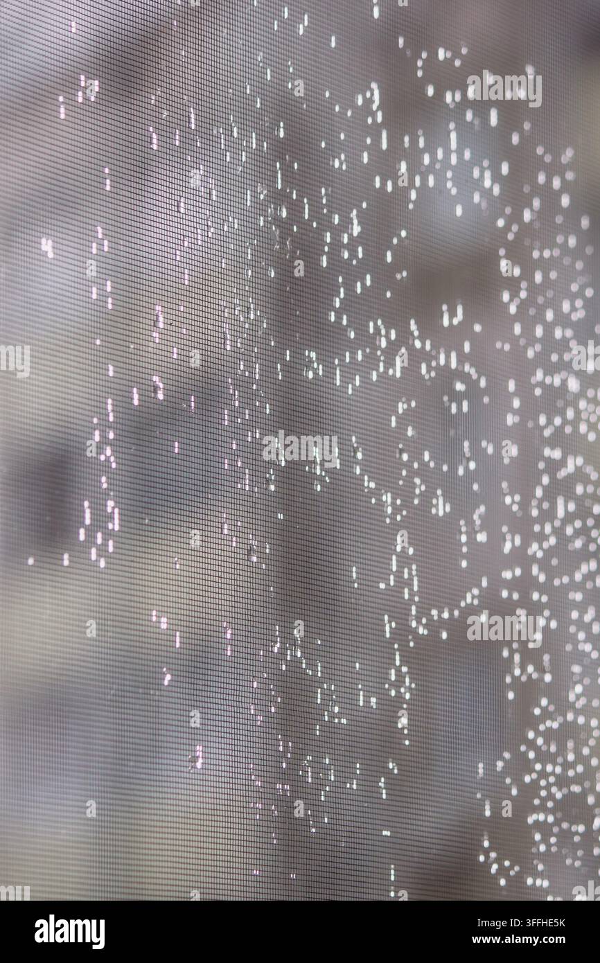 Raindrops and glowing bokeh lights on window screen mesh background Stock Photo