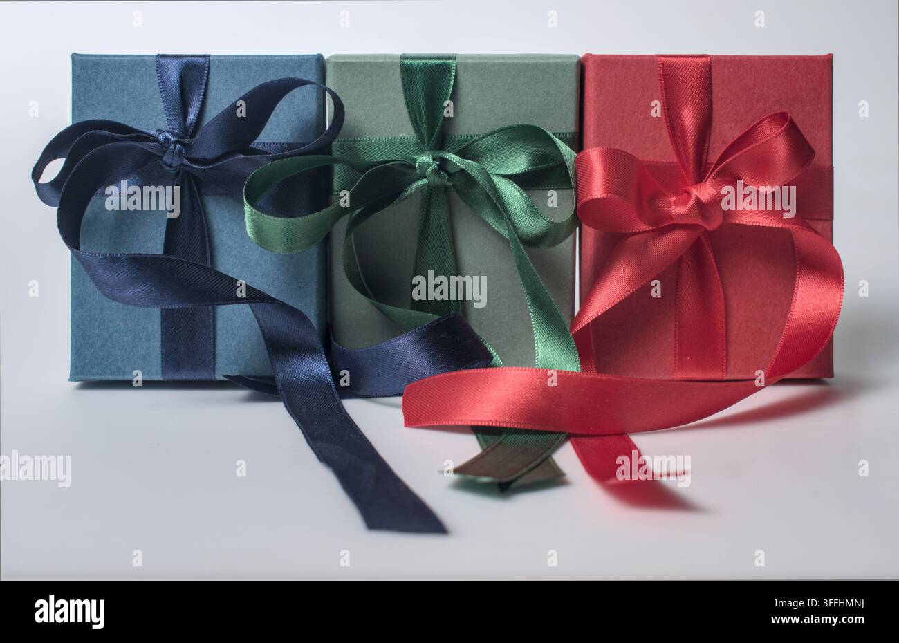 Three colored gift boxes with ribbons on white table. Stock Photo