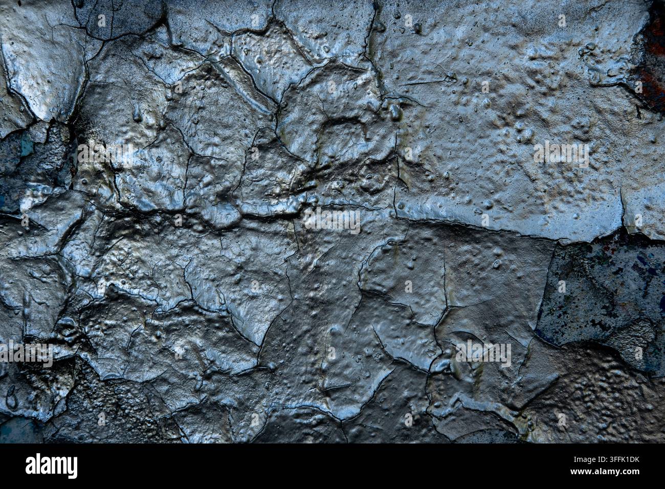 Silver peeling paint is cracking on a textured wall surface. Stock Photo