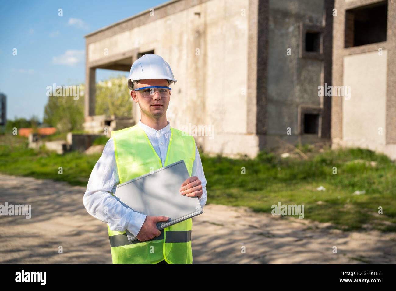Architect holding building plans at an unfinished construction site near a concrete structure. Construction project management building inspection and Stock Photo