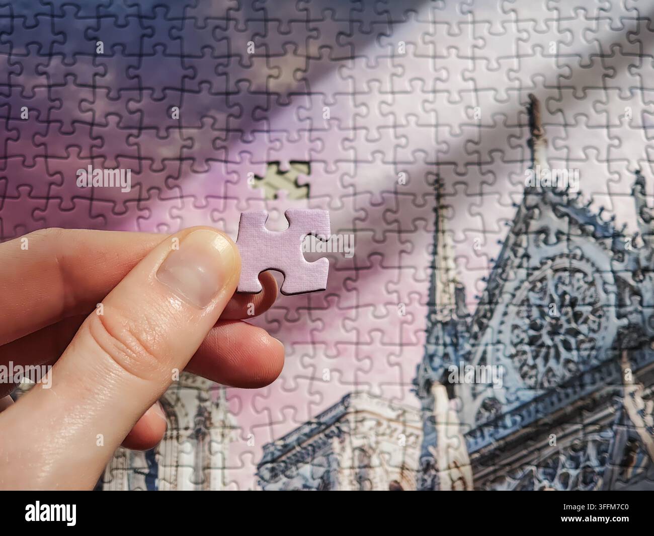 Hand inserting final missing piece into cathedral architectural jigsaw puzzle Stock Photo