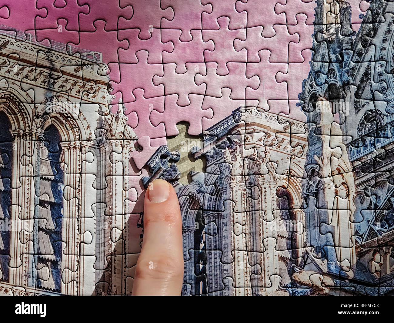 Hand inserting final missing piece into cathedral architectural jigsaw puzzle Stock Photo