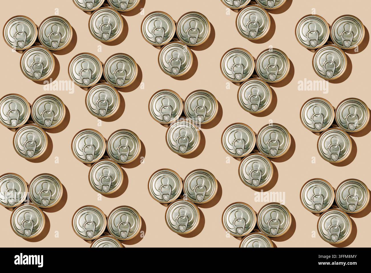 repeating triangular groups of three unopened food cans with ring pull lids create a geometric pattern on a beige background, with crisp shadows outli Stock Photo