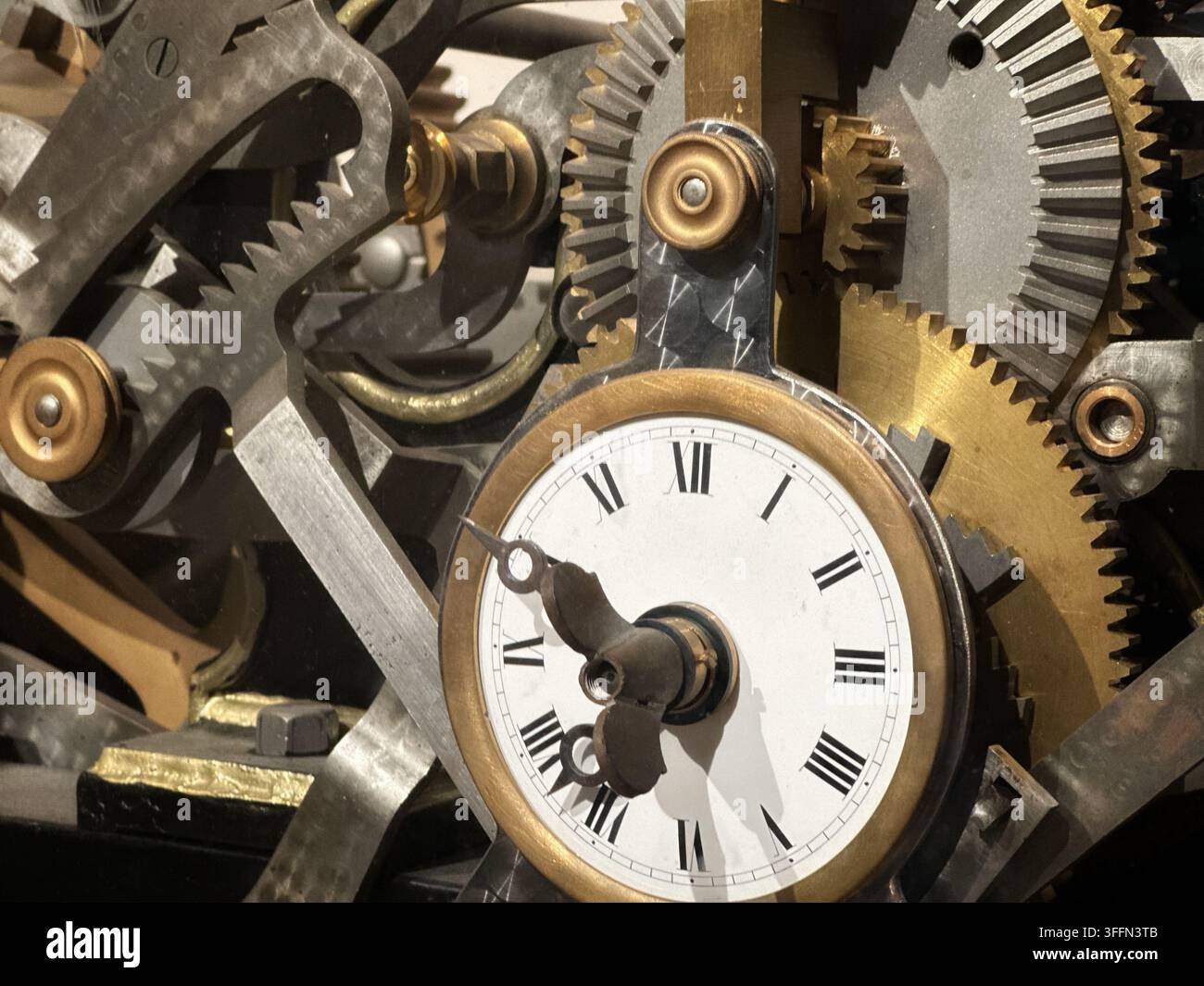 Vintage clockwork mechanism with brass gears, cogs, and a white Roman numeral dial. Intricate brass and steel clockwork gears surround a white clock f - Smartphone Captured Stock Image