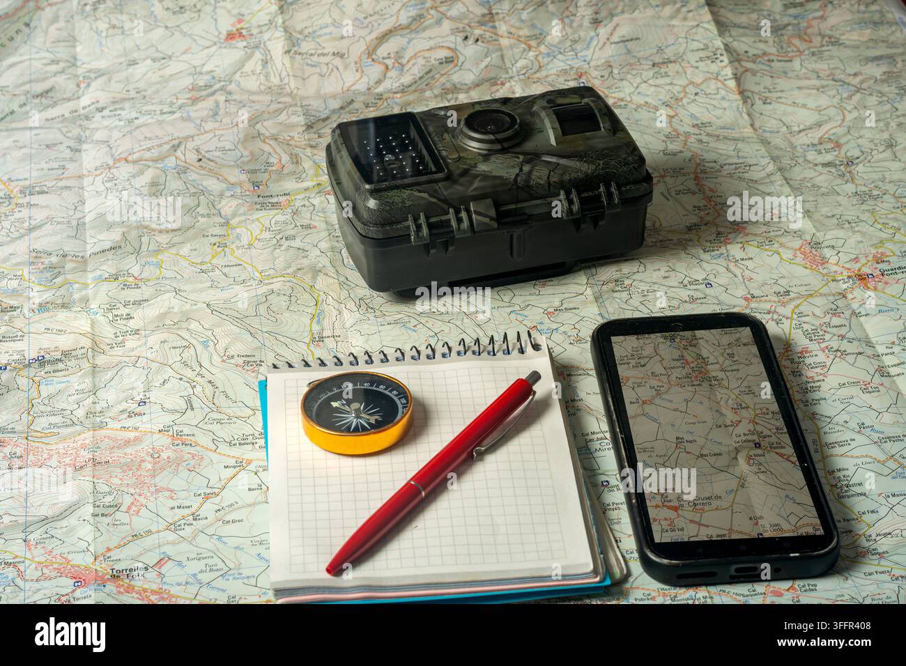 Wilderness exploration planning with map, compass, smartphone, and trail camera Stock Photo