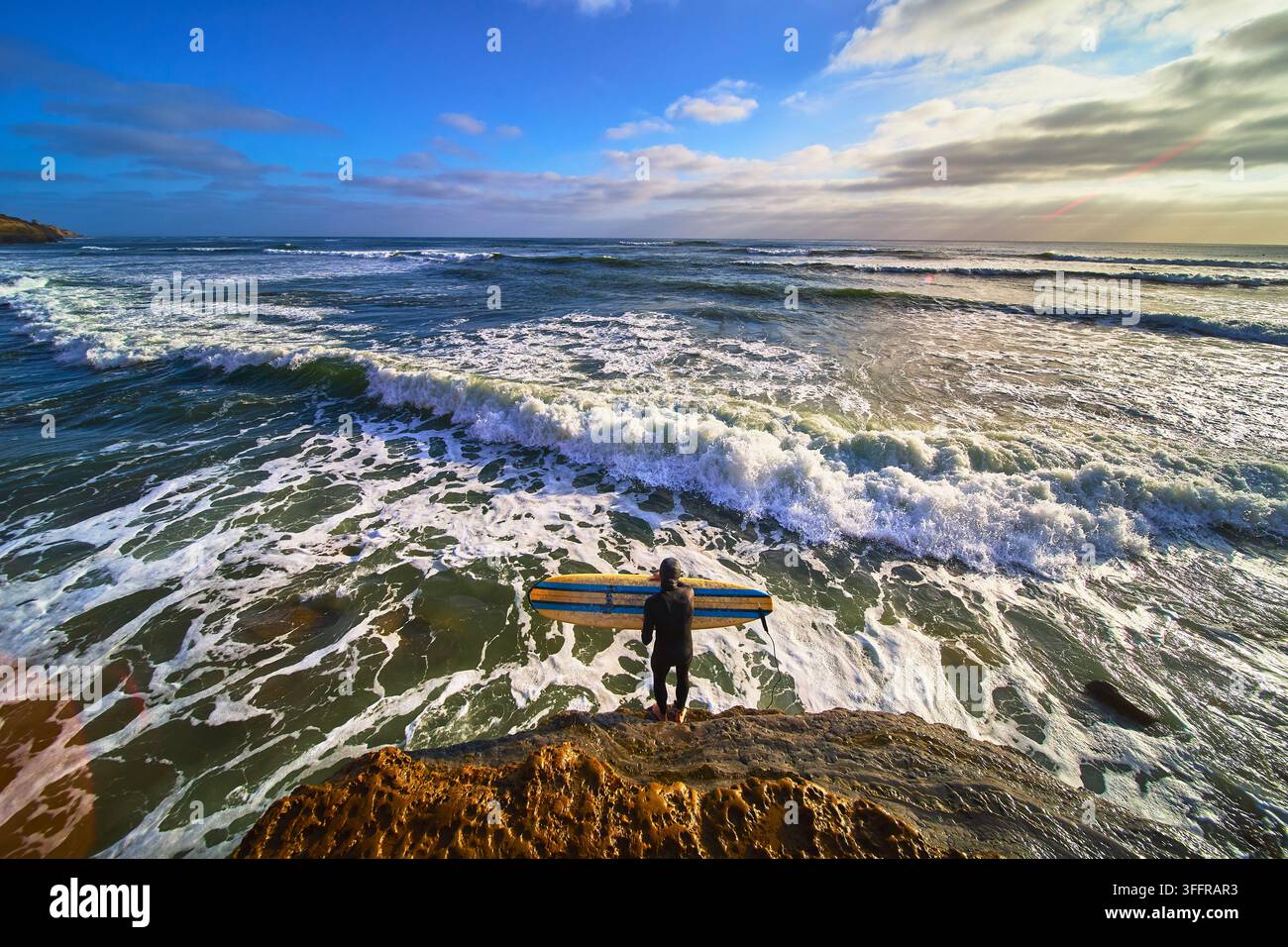 Surfer Standing on Rocky Cliff at Sunset Cliffs California Overlooking Ocean Waves Stock Photo