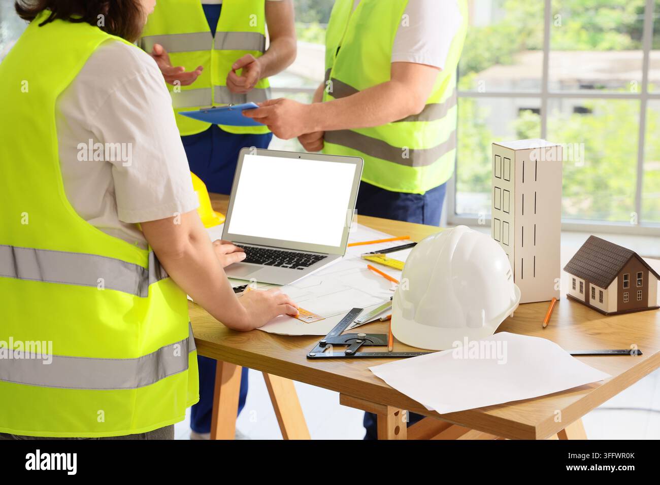 Construction project management and engineering team, architects working on building blueprints with laptop and models in a modern office workspace Stock Photo