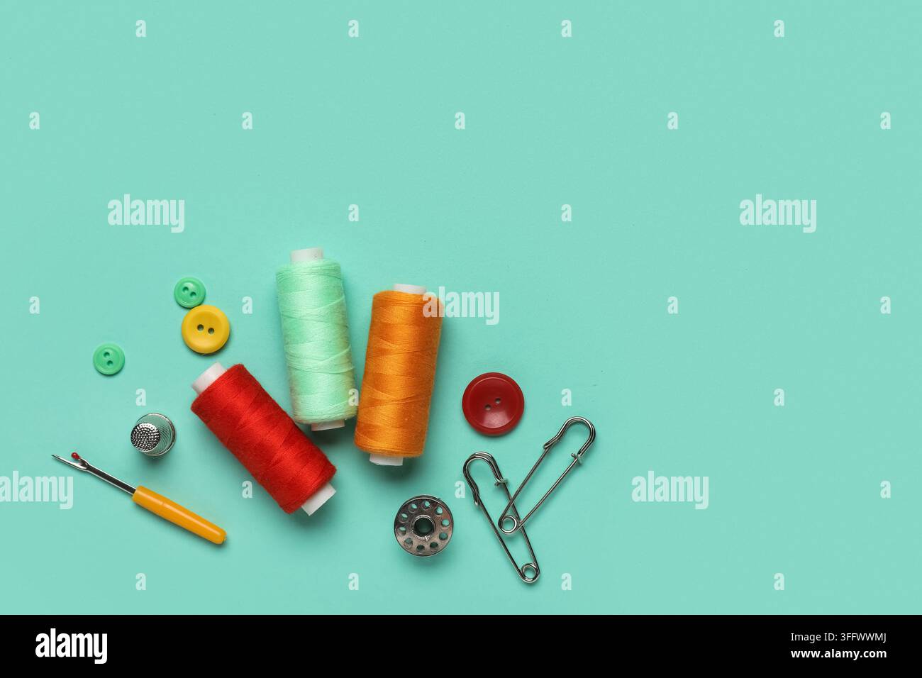 Composition with thread spools, thimble and buttons on mint background Stock Photo