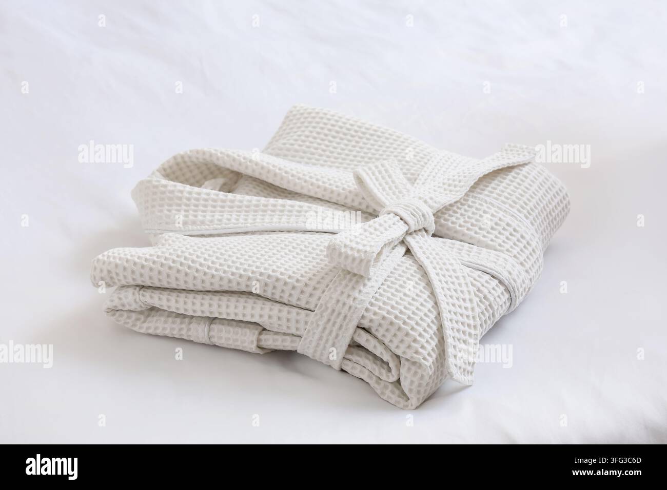 Folded waffle bathrobe on white blanket in bedroom Stock Photo