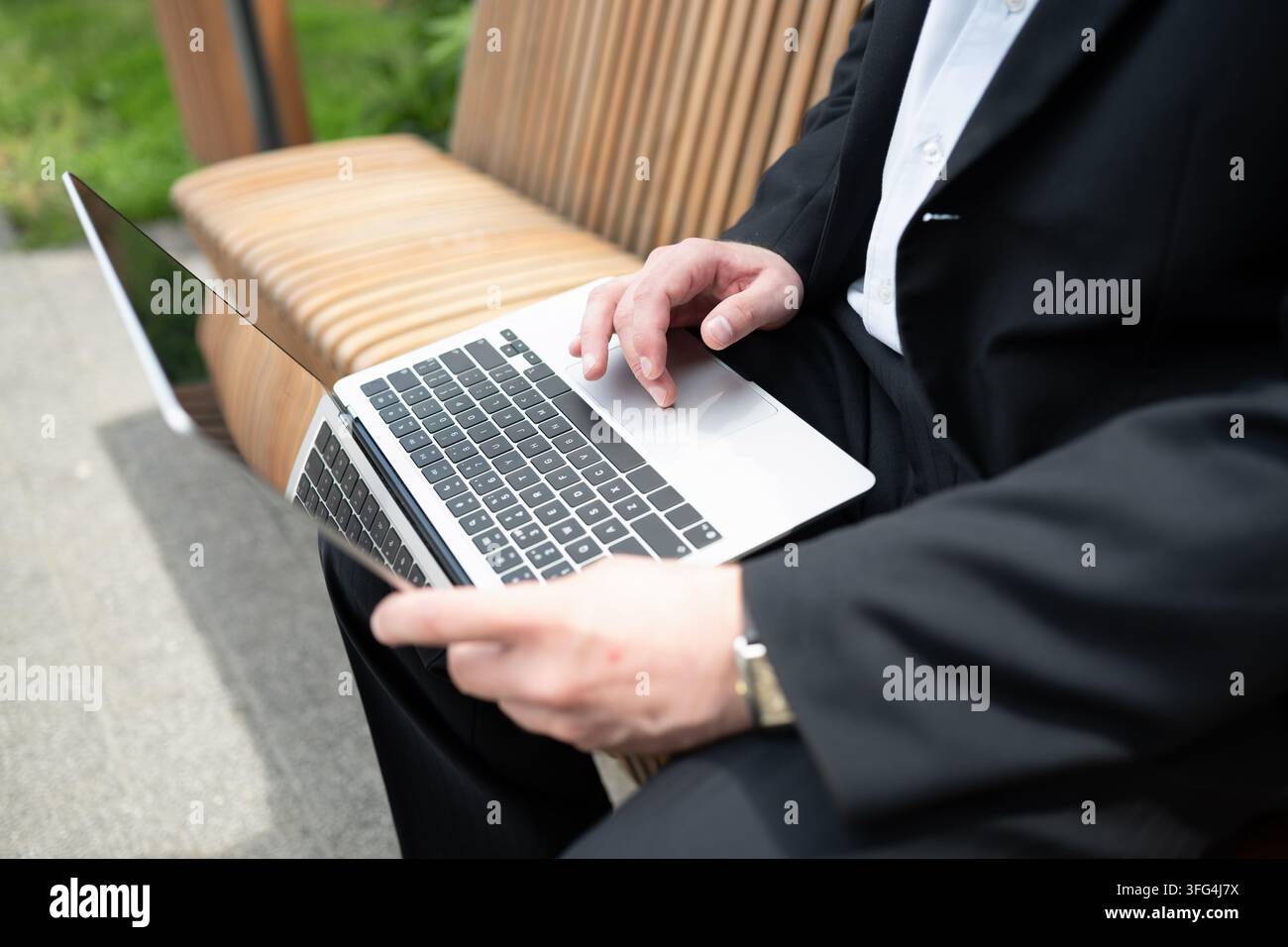 Close up of businessman using laptop while sitting on outdoor bench. Mobile office, remote work, business technology and flexible working concept. Stock Photo