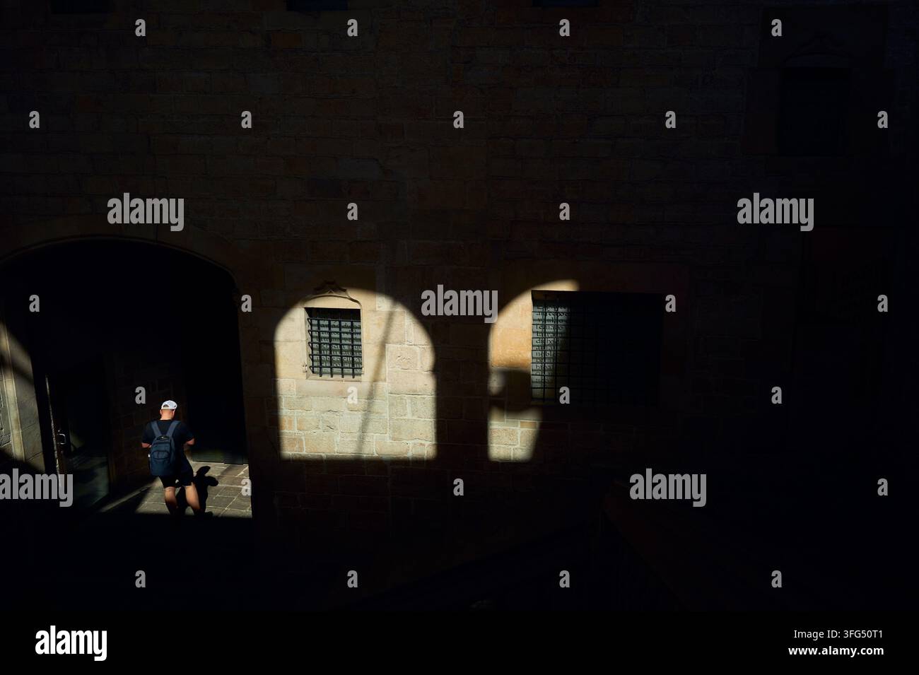 Man with backpack walks through a sunlit stone archway Stock Photo