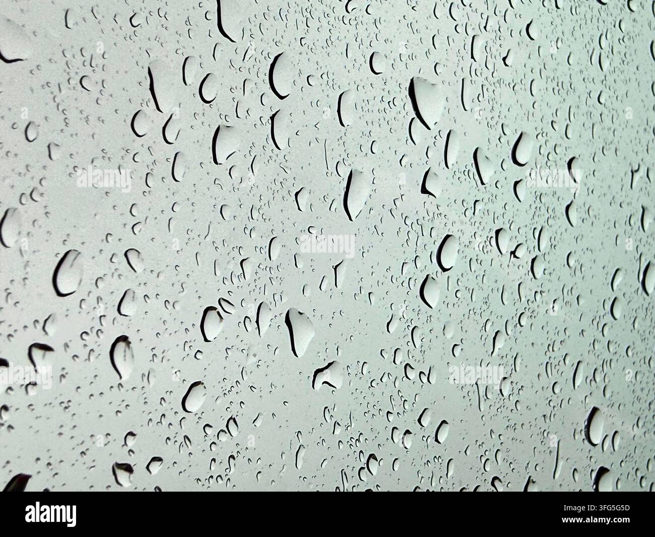 Close-up macro photo of water droplets and rain trails on a glass surface against a soft light background. Stock Photo