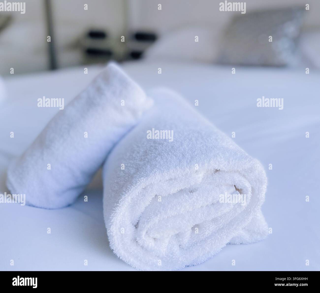 Fresh rolled white bath towels arranged neatly on a clean white bed sheet. Stock Photo