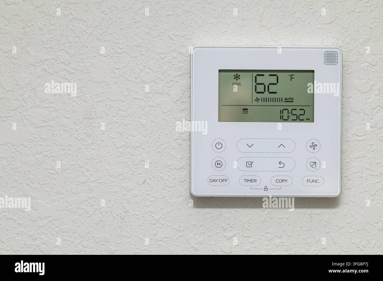 Wall-mounted air conditioning controller displaying 62°F in cool mode, featuring timer and fan settings on textured interior wall. Stock Photo