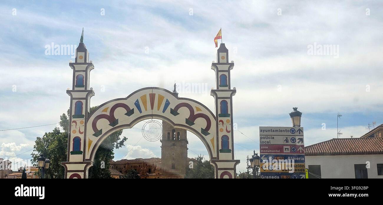 Decorative illuminated fair arch near Plaza de la Constitución with Guadix Cathedral tower visible behind during the Feria y Fiestas de Guadix 2026. G - Smartphone Captured Stock Image