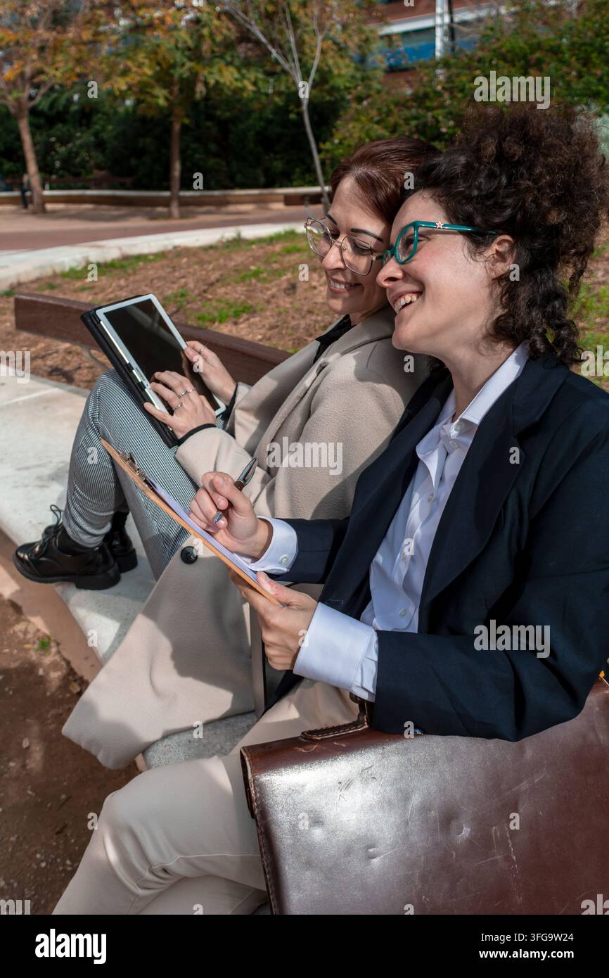 Businesswomen collaborating outdoors using tablet and clipboard Stock Photo