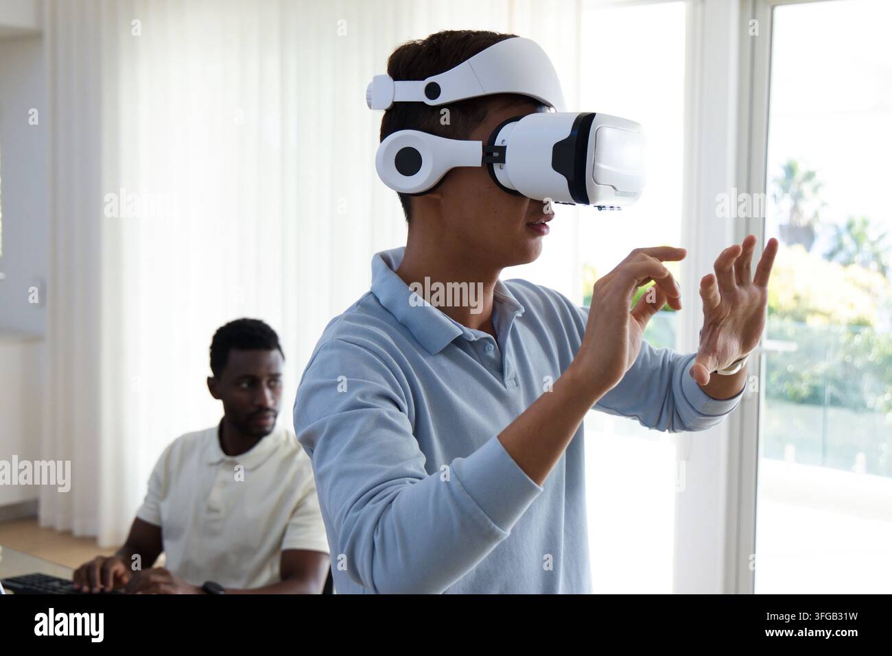 Diverse male coworkers testing VR interface in bright home office with white headset, keyboard Stock Photo