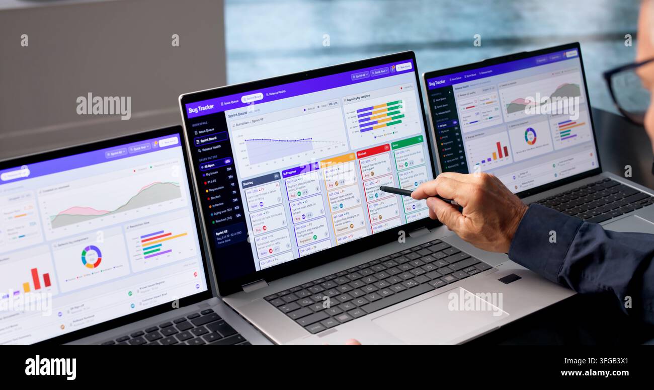 Software Developer Reviews Bug Tracking Dashboard On Laptop During Sprint. Stock Photo