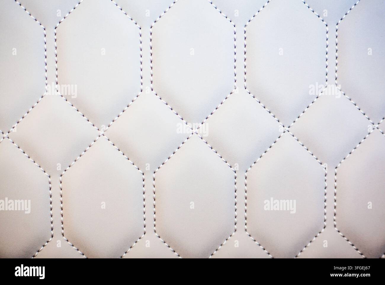 Close-up macro view of white quilted faux leather upholstery with a geometric stitched hexagonal and diamond pattern, Portugal Stock Photo