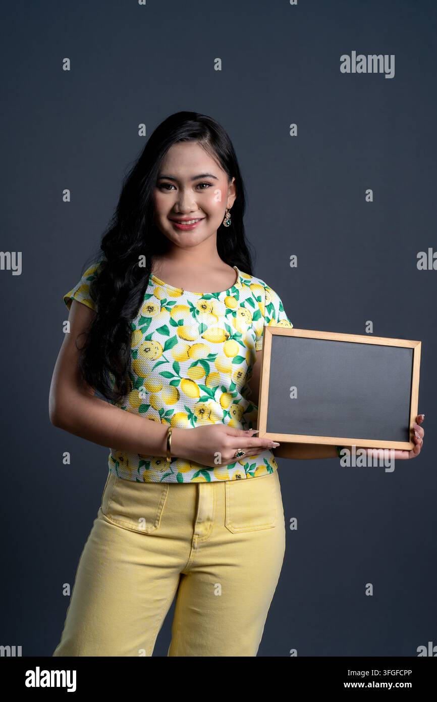 Portrait of young woman holding a blank blackboard in yellow theme cloth Stock Photo