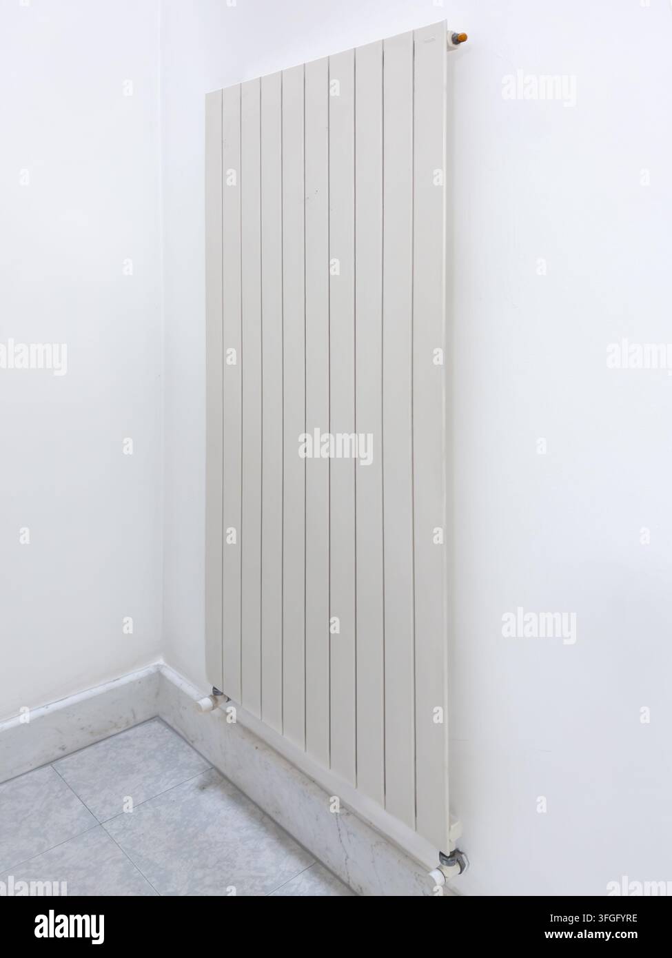 Side view of a sleek, white vertical flat-panel radiator installed on a clean white wall in a modern room with marble flooring. Perfect concept for co Stock Photo