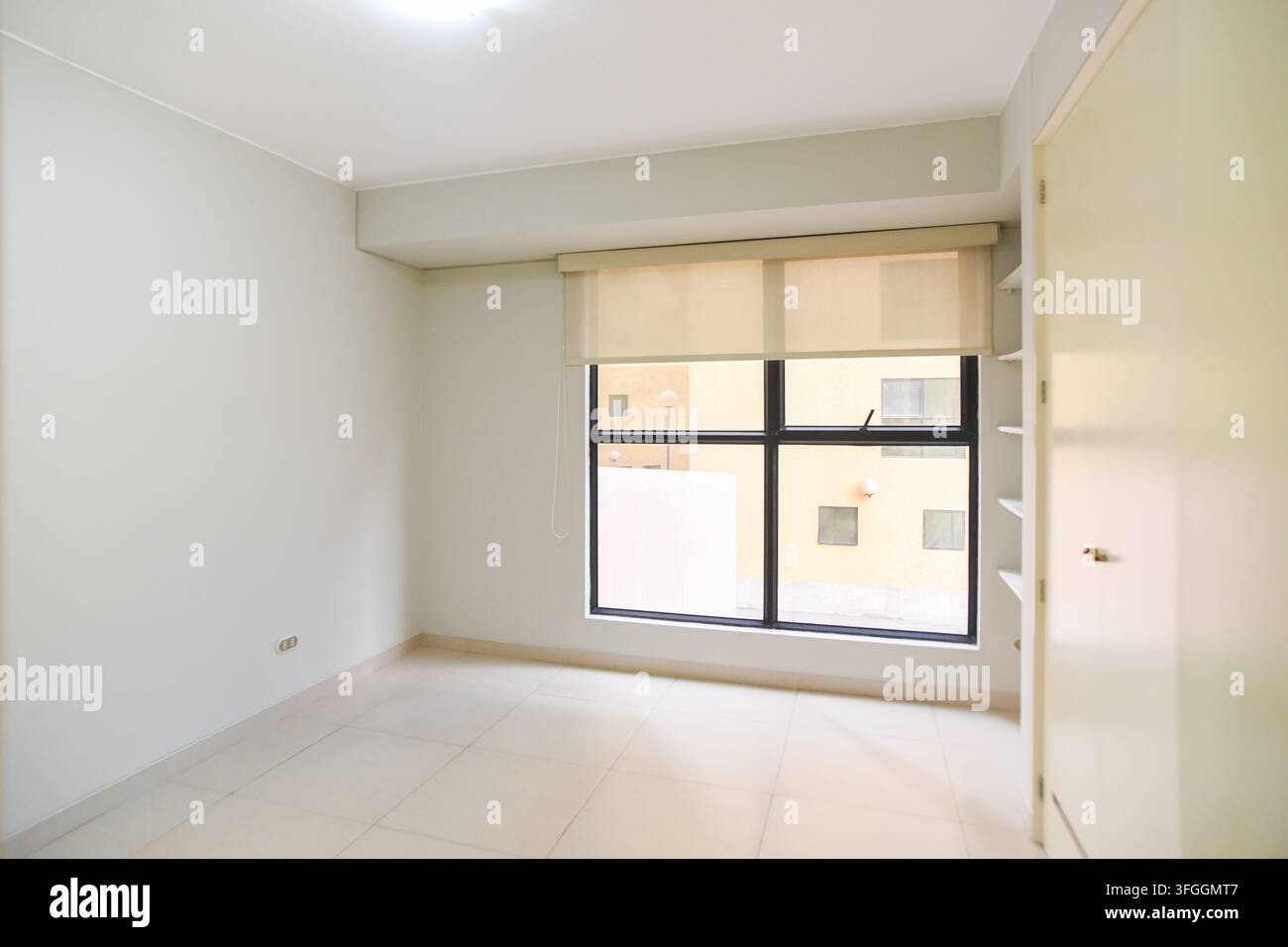 Empty Room with Window: An empty, minimalist room features a large window offering a view of an urban landscape, complemented by a closet and built-in Stock Photo