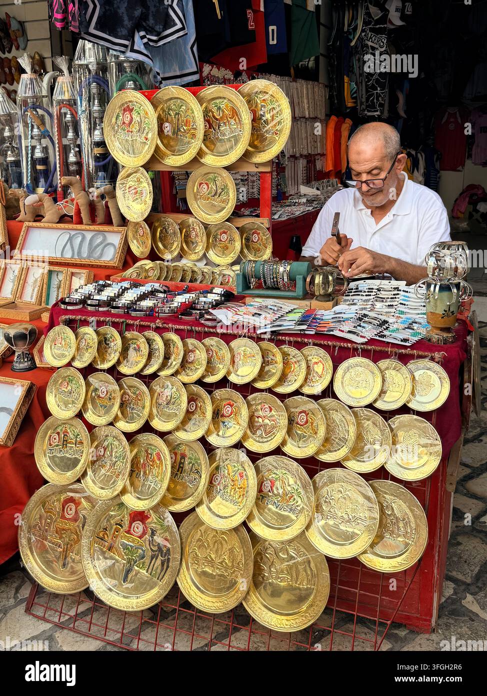 Tunisian artisan engraving traditional brassware at his market stall in the historic Medina of Sousse, Tunisia. - Smartphone Captured Stock Image