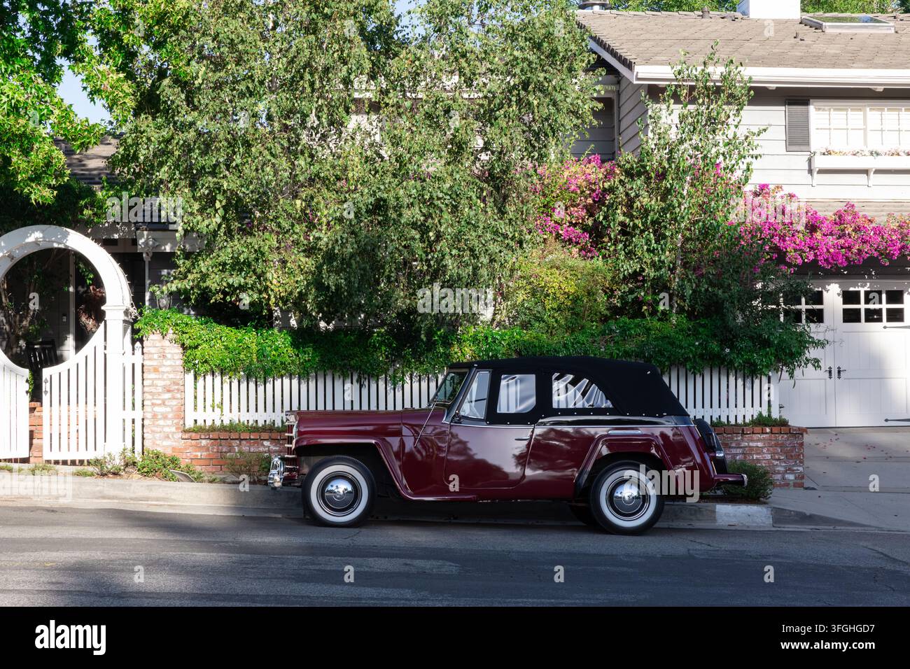 Los Angeles, California, USA - September 12, 2026: Vintage burgundy car parked along residential street beside landscaped home, white fence, brick wal Stock Photo