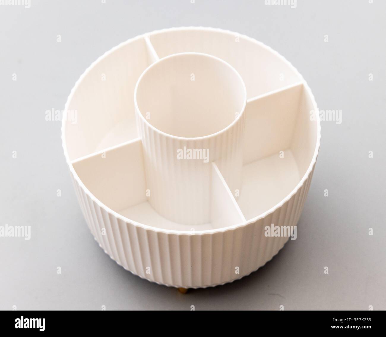 A creamcolored round plastic organizer with multiple compartments on a grey background Stock Photo