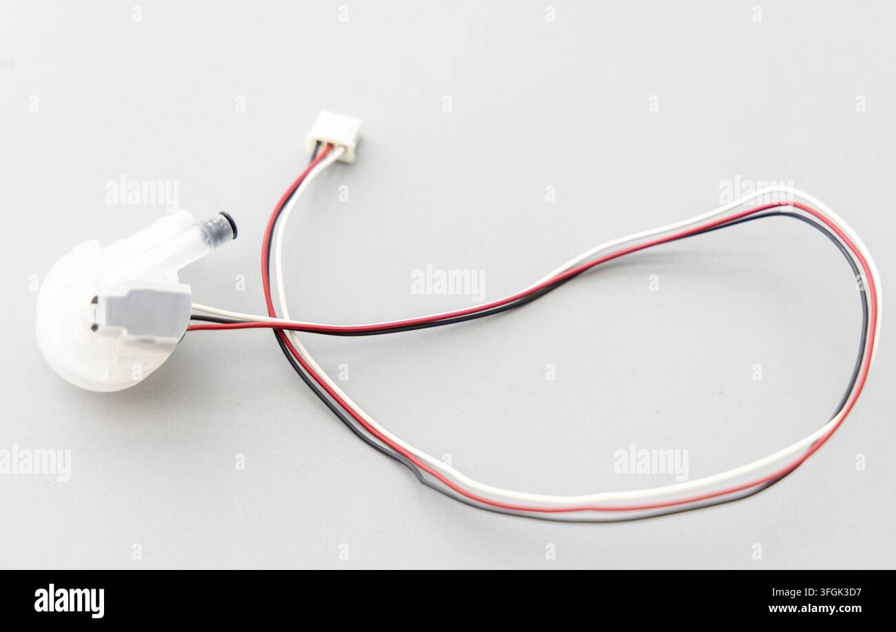 A white electronic component with colored wires sits on a grey surface Stock Photo