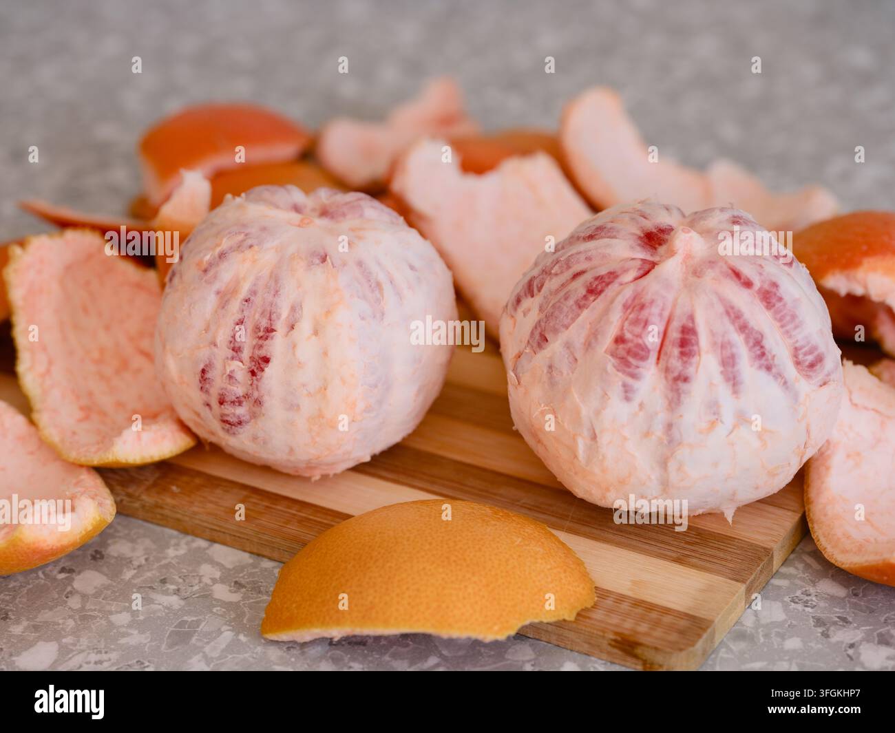 Two peeled whole grapefruits on a wooden cutting board surrounded by pieces of citrus peel. Stock Photo