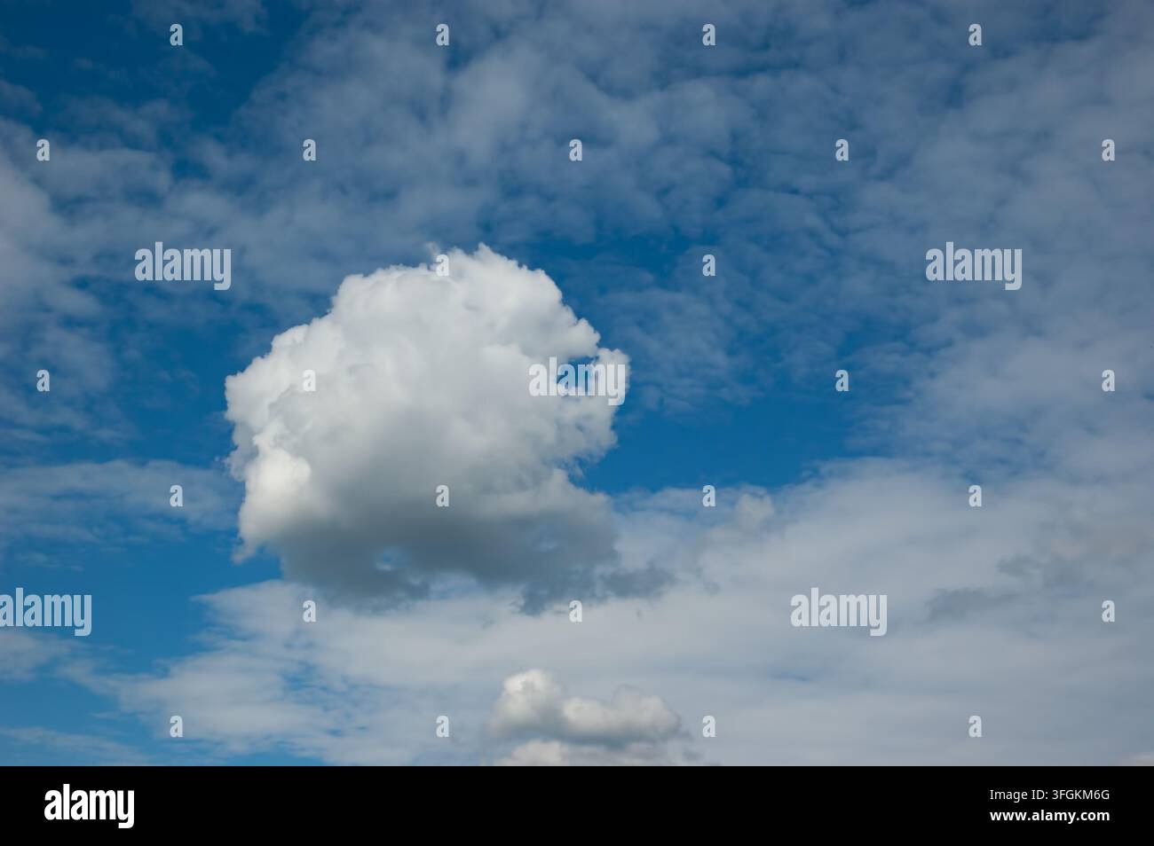 Blue sky with fluffy white clouds and a single distinctive cloud with an unusual shape. Stock Photo