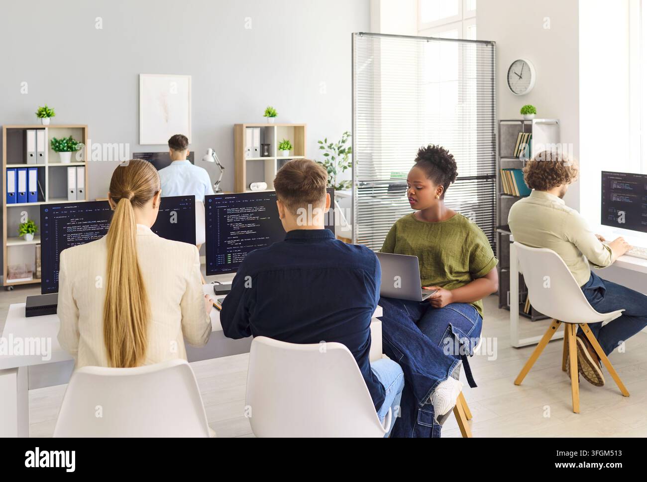 Developers collaborating in modern office, coding software on computers together Stock Photo