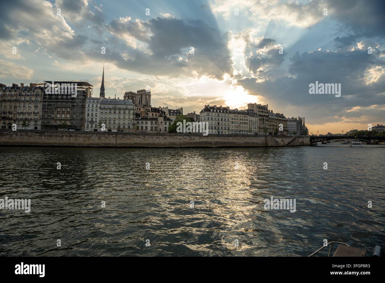 Panoramic view of the Seine River, Île de la Cité, and Notre-Dame spire framed by dramatic sunbeams bursting through clouds at sunset in Paris, France Stock Photo