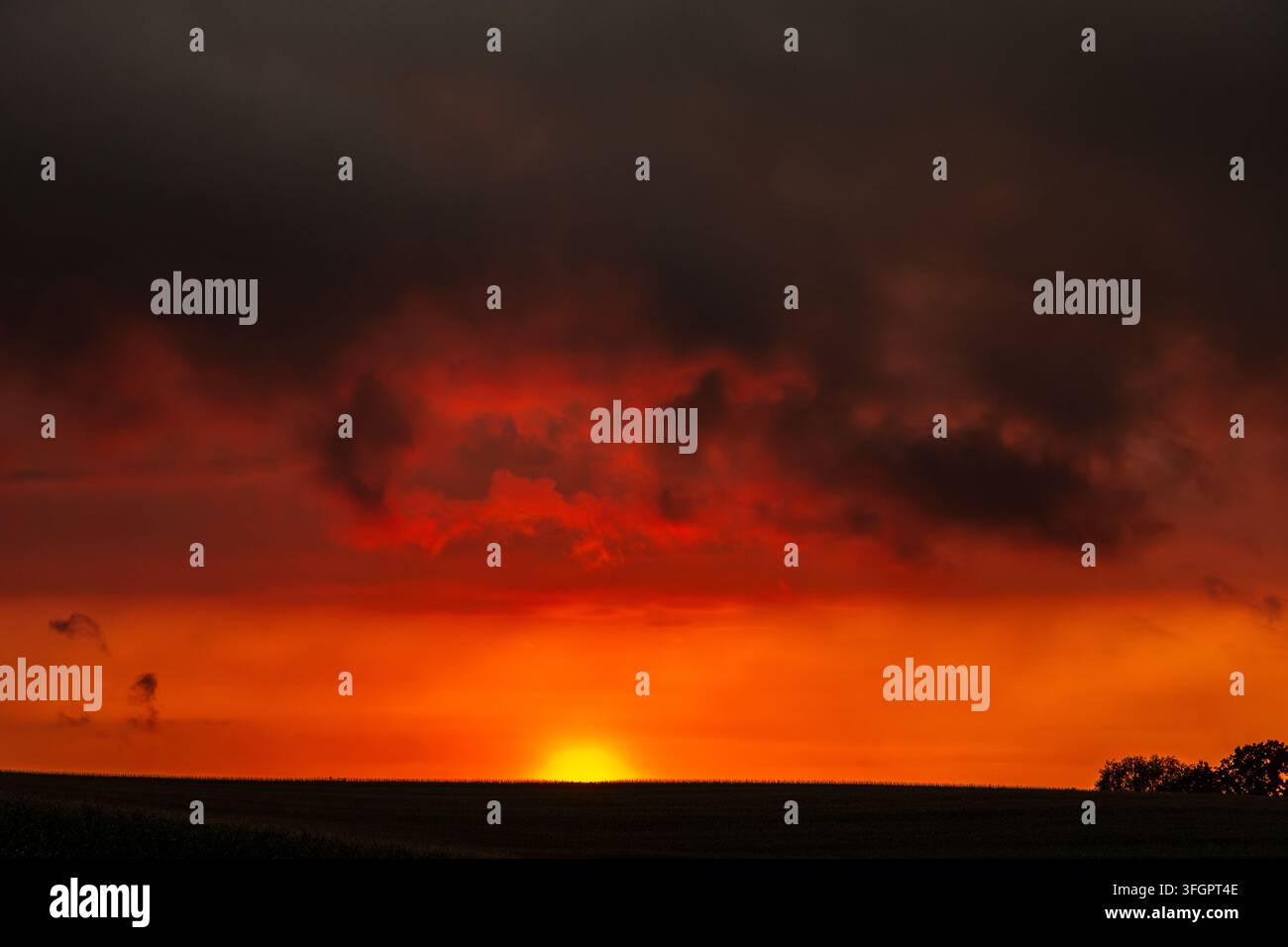 Dramatic orange sunset beneath dark storm clouds over a quiet rural horizon Stock Photo