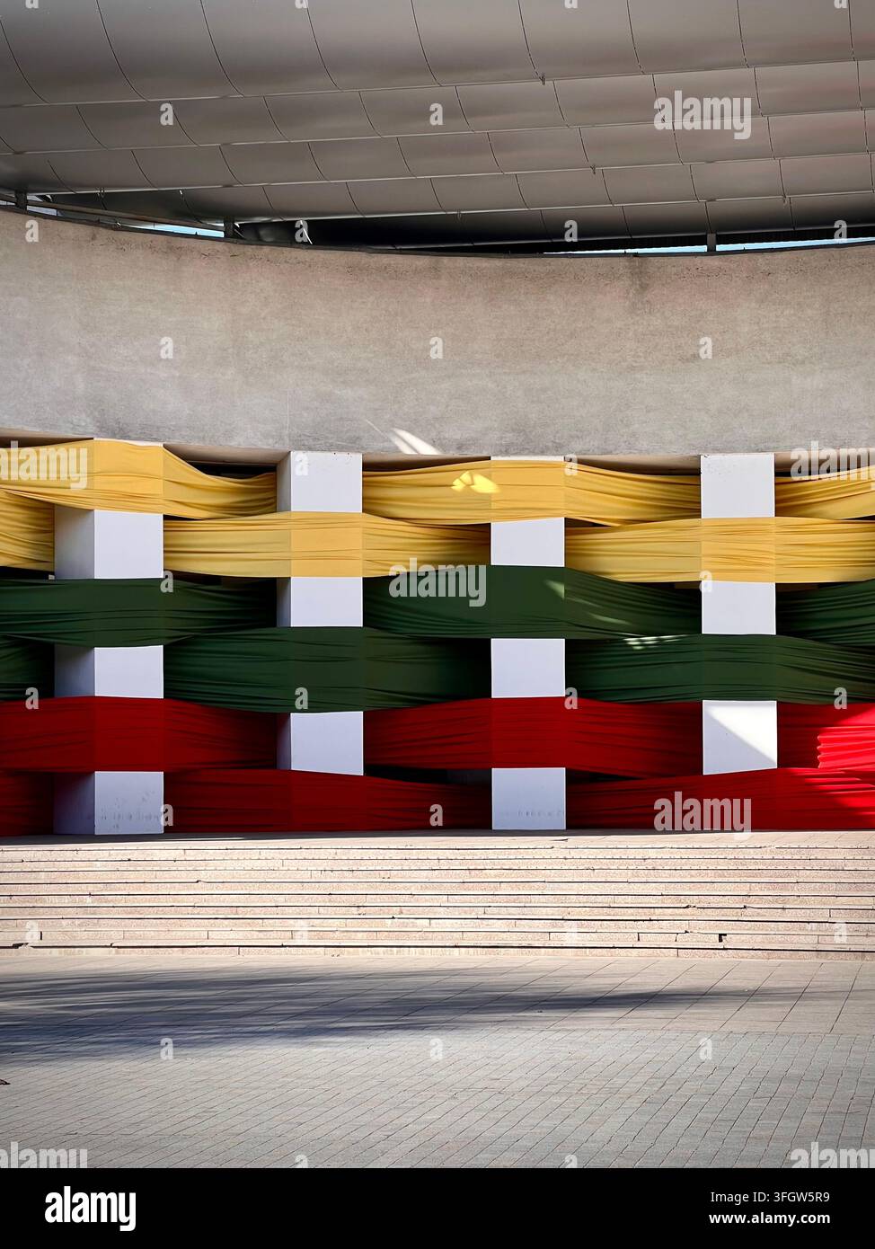 Vertical photograph of a fabric art installation displaying the Lithuanian flag woven through pillars at the Alytus Amphitheater. - Smartphone Captured Stock Image