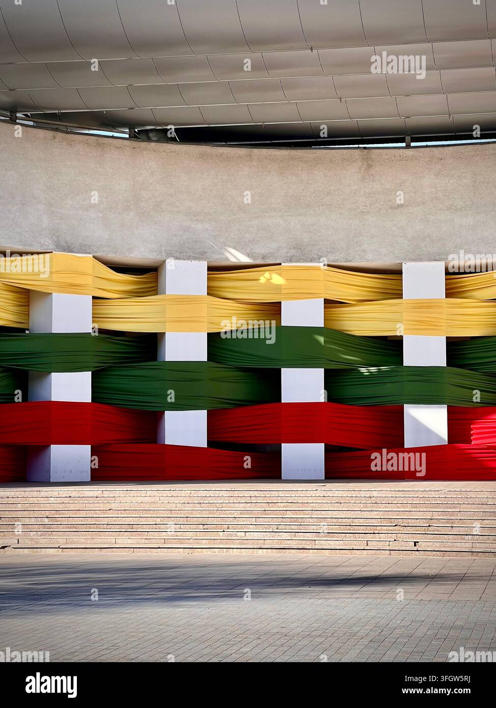 Vertical photograph of a fabric art installation displaying the Lithuanian flag woven through pillars at the Alytus Amphitheater. - Smartphone Captured Stock Image