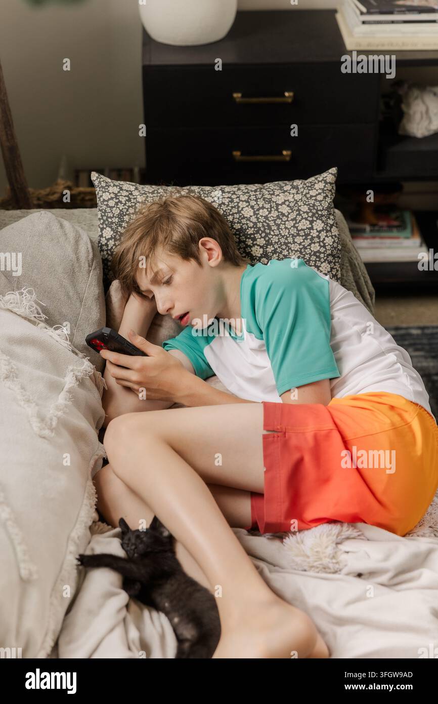 Boy lounges on couch using his smartphone Stock Photo
