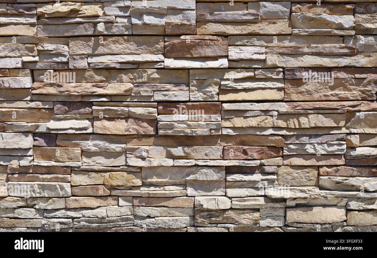 External wall coating made of stacked bricks of yellow, brown, beige and white stones. Panels for exterior. Background and texture. Stock Photo