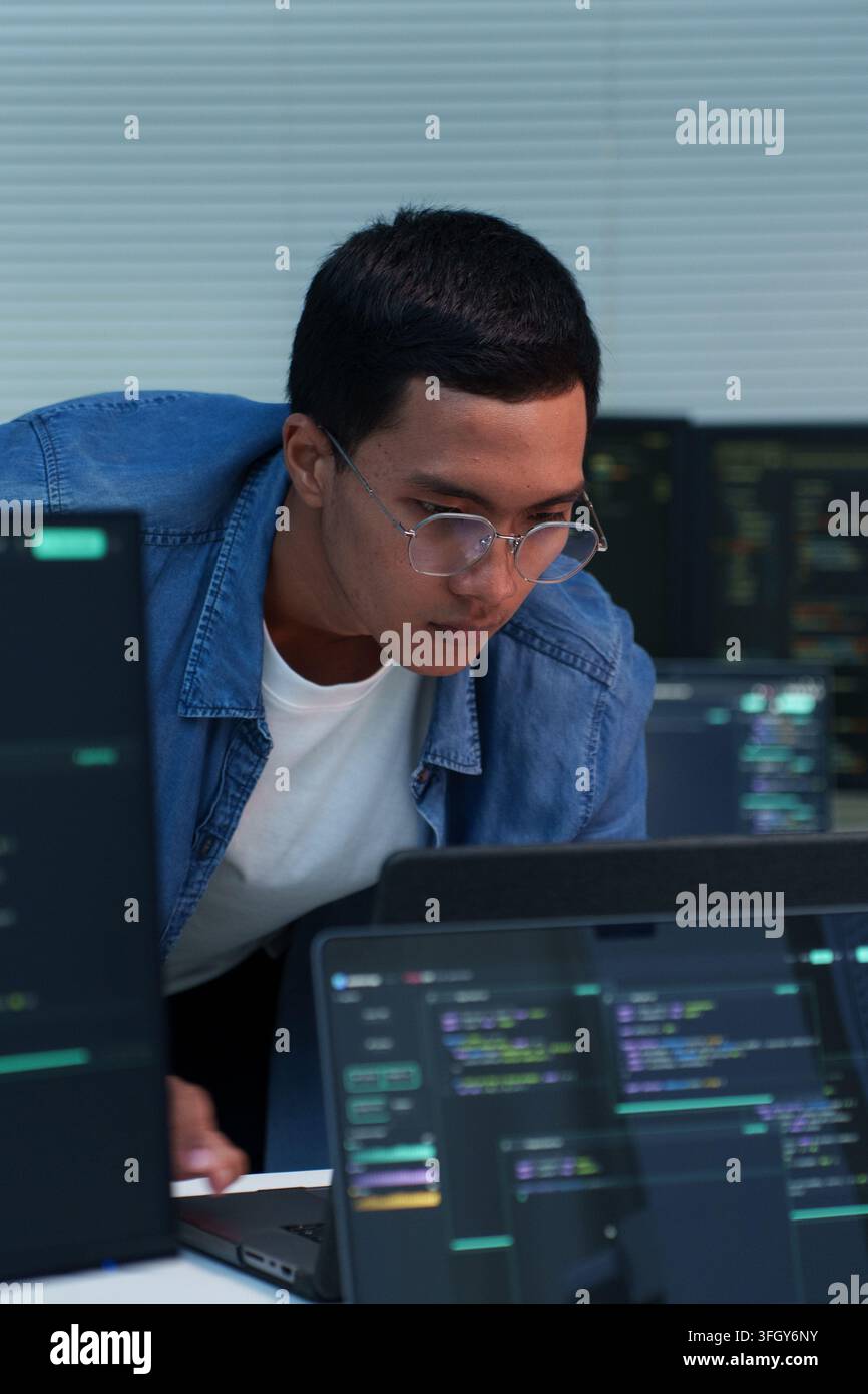 Focused young programmer analyzing source code and developing digital software with laptops, supporting programming, artificial intelligence, cybersec Stock Photo